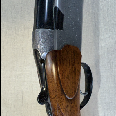 Arma de caça com empunhadura de madeira castanha e detalhes gravados em metal prateado