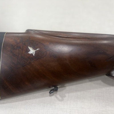 Coronha de espingarda em madeira escura com entalhe de pássaro branco e detalhes florais