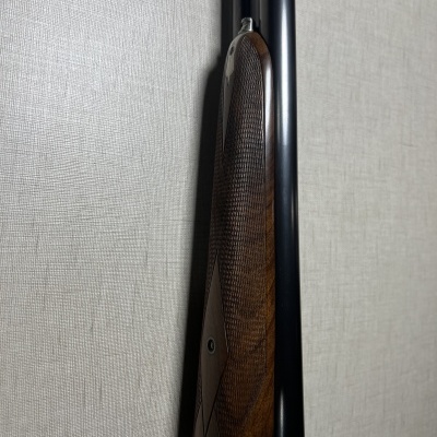 Espingarda com coronha em madeira e cano preto encostada a parede.