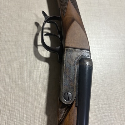 Parte de espingarda com madeira, metal preto e prateado, com padrões gravados