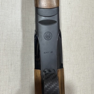 Detalhe de arma de fogo com madeira, metal preto e fibra de carbono