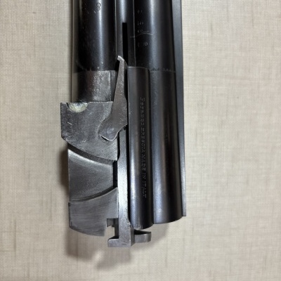Detalhe do cano de uma arma de fogo em metal preto com texto Perazzi BRESCIA MADE IN ITALY