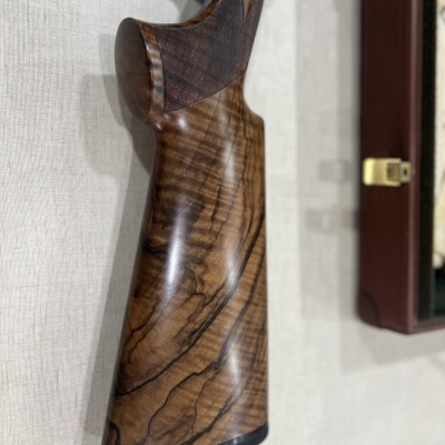 Parte traseira de uma arma em madeira castanha polida pendurada na parede junto a uma caixa de madeira.