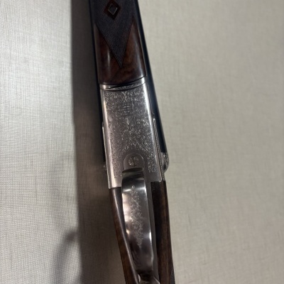 Espingarda de caça com madeira e aço gravado sobre fundo bege.