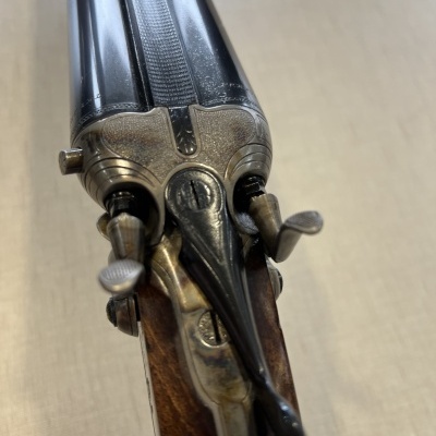 Espingarda de canos duplos lado a lado com coronha de madeira.