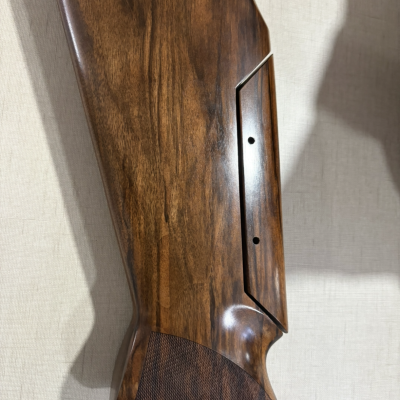 Coronha de arma de fogo em madeira castanha com textura polida e antiderrapante, detalhe em preto na extremidade.