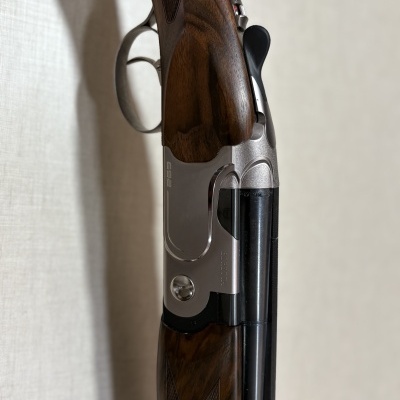 Espingarda de canos duplos com madeira e metal prateado encostada numa parede clara