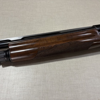 Detalhe de arma de fogo com acabamento em madeira castanha e partes metálicas pretas