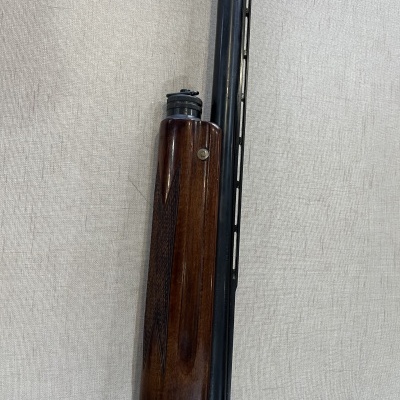 Espingarda com coronha de madeira castanha e cano preto sobre tecido bege.