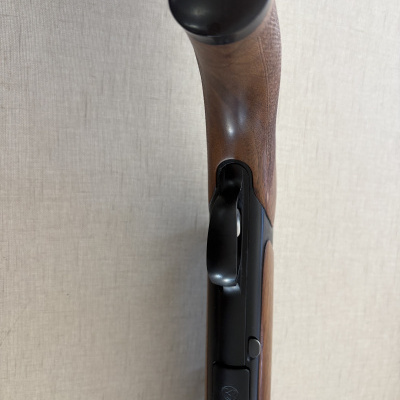 Detalhe do cabo em madeira e parte metálica de arma de fogo com símbolo dourado.