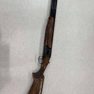 Espingarda com madeira castanha e cano preto contra tecido cinzento