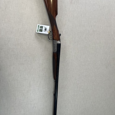 Espingarda de caça com cornos em madeira e canos duplos pretos pendurada numa parede clara