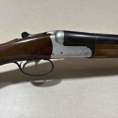 Espingarda de caça beretta com canos duplos pretos e punho em madeira escura com gravações e texto.