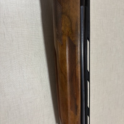 Parte frontal da arma de fogo com coronha de madeira castanha e detalhes gravados