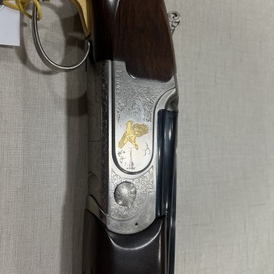 Espingarda canos duplos com madeira escura e gravações metálicas douradas e prateadas