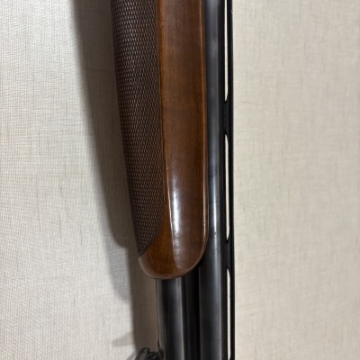 Parte de um fuzil com coronha em madeira castanha e canos metálicos pretos