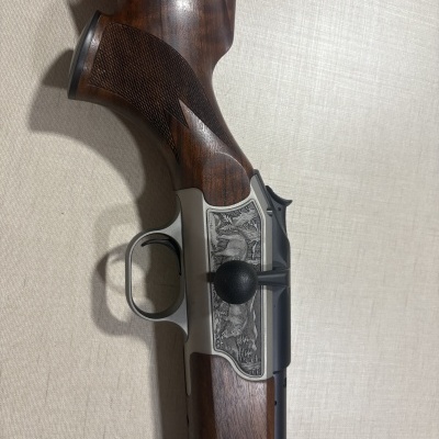 Rifle de caça com coronha em madeira castanha e caixa metálica prateada com gravuras de animais.