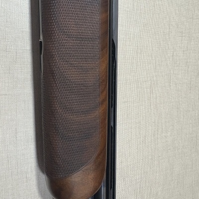 Parte de arma de madeira castanha com textura trapezoidal encostada em superfície clara