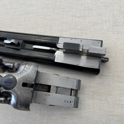 Parte desmontada de arma de fogo metálica prateada e negra sobre tecido bege