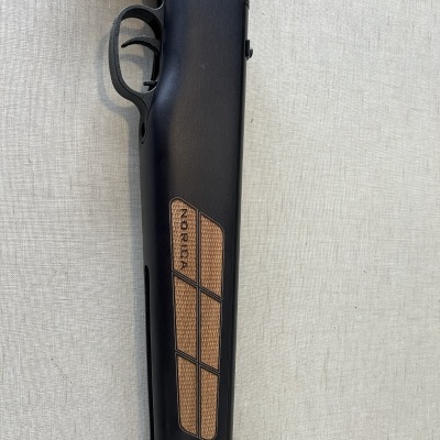 Espingarda preta com detalhes em madeira castanha e texto NORICA