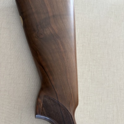 Parte traseira de arma de madeira castanha com textura quadriculada e borracha preta no topo