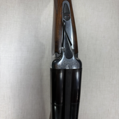 Espingarda de canos duplos com coronha de madeira castanha e detalhes metálicos gravados.