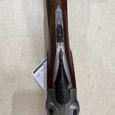 Parte superior de rifle com coronha de madeira escura e detalhes metálicos prateados gravados