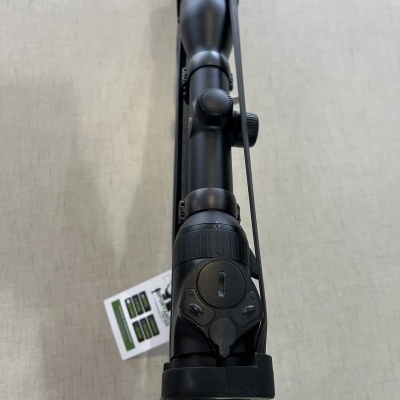 Mira telescópica preta montada numa arma com etiqueta branca ao lado