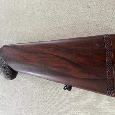 Espingarda com madeira castanha escura e textura quadriculada sobre tecido bege