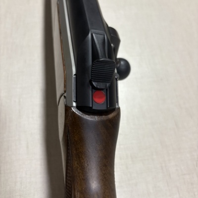 Rifle com coronha em madeira castanha e metal preto com botão vermelho