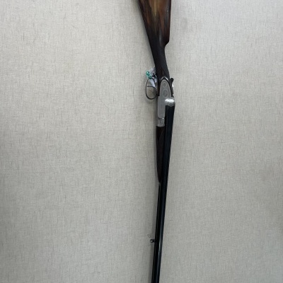 Espingarda com coronha de madeira e canos paralelos encostada a uma parede clara