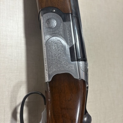 Espingarda com madeira castanha e ação metálica prateada com gravações florais.