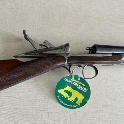 Espingarda dupla com coronha em madeira e canos metálicos, etiqueta verde pendurada