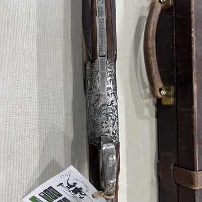 Rifle de cano duplo com detalhes em madeira e gravações em metal prateado ao lado de mala de couro