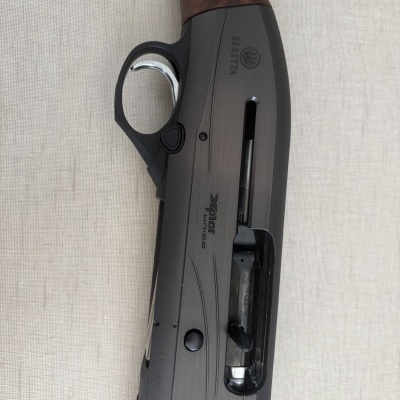 Espingarda Beretta com empunhadura em madeira e corpo preto com texto BERETTA e XPLOR unico sobre fundo bege.