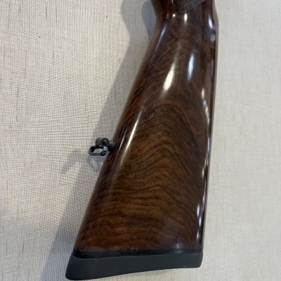 Coronha castanha escura de espingarda de caça em madeira polida na parede clara.