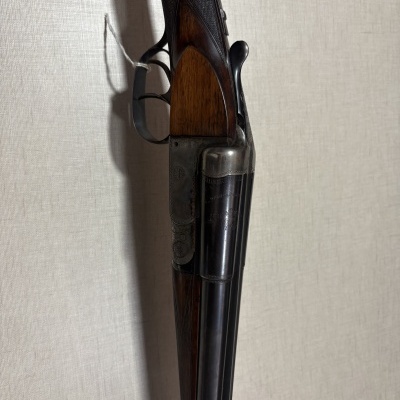 Espingarda de canos duplos em metal negro e madeira escura com textura quadriculada.
