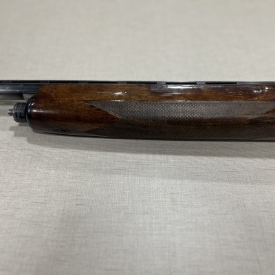 Parte do cabo de arma em madeira castanha com textura quadriculada e tubo metálico preto