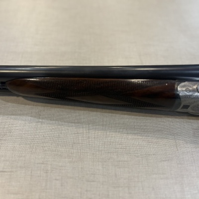 Espingarda canos duplos metal negro e massa de madeira castanha sobre tecido bege