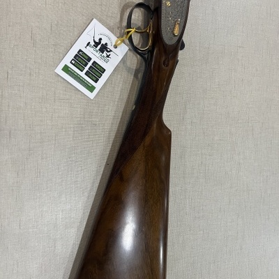 Espingarda de canos duplos com coronha em madeira escura polida e gravações na parte metálica.