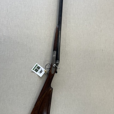 Espingarda dupla em madeira escura com canos pretos e etiqueta pendurada