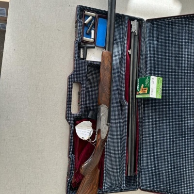 Rifle de caça com cano duplo em estojo com acessórios sobre mesa clara.