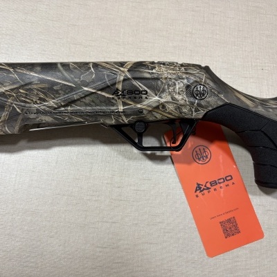 Espingarda camuflada Beretta AX800 Suprema com pega preta e etiqueta laranja sobre fundo bege.