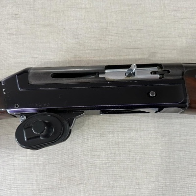 Espingarda com corpo metálico preto e partes em madeira castanha sobre fundo têxtil claro