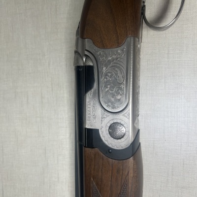 Espingarda Beretta em metal prateado e madeira castanha, com gravações e texto visível