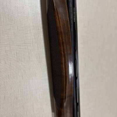 Espingarda com madeira castanha e cano preto encostada numa parede beige.