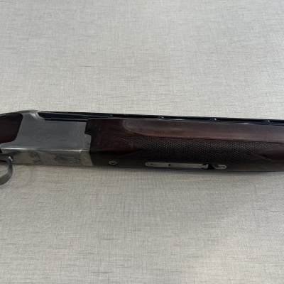 Espingarda over and under com madeira castanha e metal prateado sobre superfície cinzenta