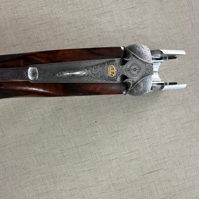 Espingarda com detalhes gravados e coroa dourada sobre tecido bege