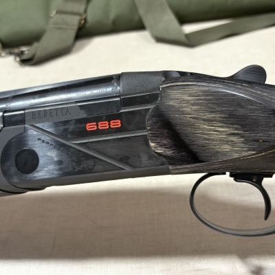 Espingarda Beretta modelo 688 em metal preto e madeira cinza escura com gravações e detalhes em relevo.