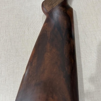 Cabo traseiro de arma de fogo em madeira escura e borracha preta sobre superfície clara